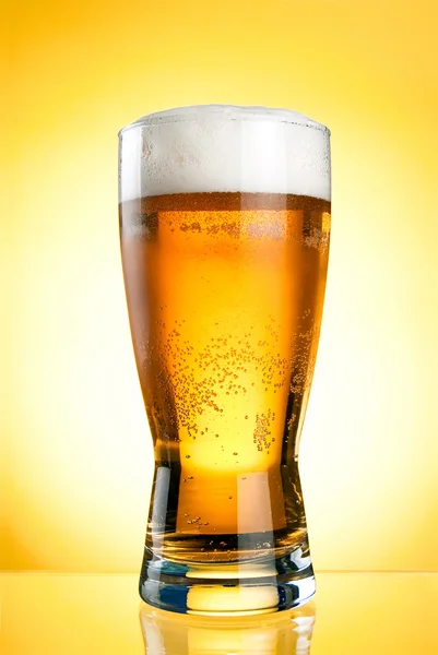 Copo de cerveja close-up com espuma sobre fundo amarelo — Fotografia de Stock