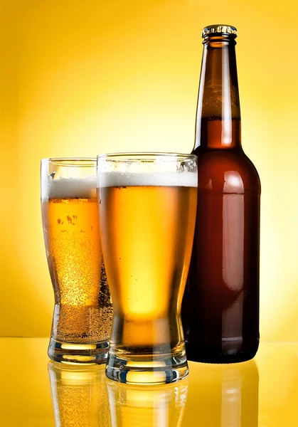 Dvě sklenice a láhev čerstvé světlé piva na žlutém podkladu — Stock fotografie