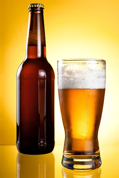 Jedna sklenička a láhev čerstvé světlé piva na žlutém podkladu — Stock fotografie