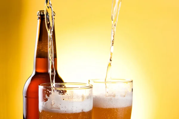 Пиво наливают в два бокала и бутылку на желтом фоне — стоковое фото
