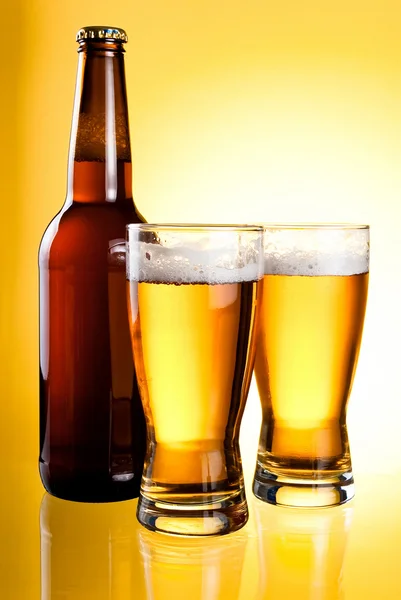 Δύο ποτήρια και μπουκάλι φρέσκιας μπίρας φως σε κίτρινο φόντο — Φωτογραφία Αρχείου