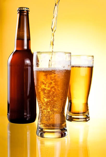 Birra versata in due bicchieri e bottiglia su sfondo giallo — Foto Stock
