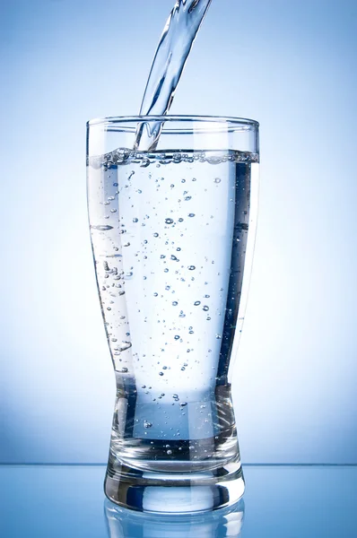 Versare l'acqua nel vetro su uno sfondo blu — Foto Stock