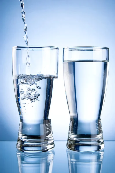 Вливание воды в стакан и стакан воды на голубой бэкгру — стоковое фото