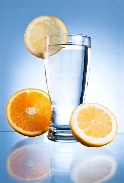 Glass of water, lemon and orange on a blue background — Stock Photo, Image