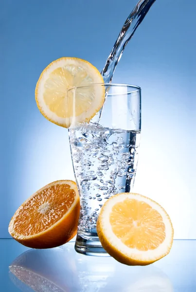 Vaso de agua mineral con limón y naranja sobre fondo azul — Foto de Stock