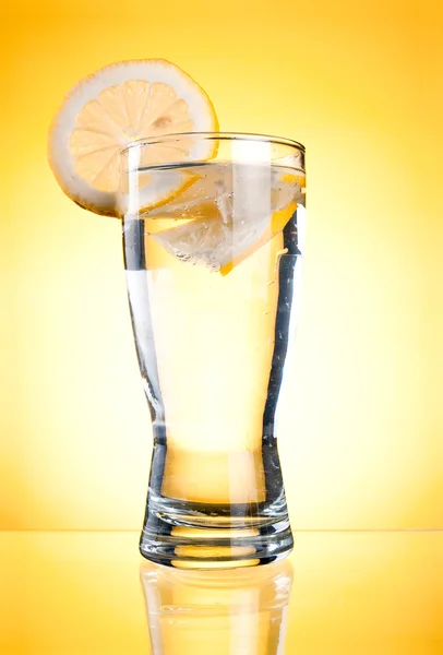 Mineral water in glass with a lemon on a yellow background — Stock Photo, Image