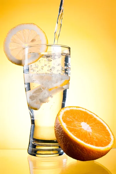 Pouring of mineral water in glass with a lemon and orange on a y — Stock Photo, Image