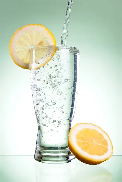 Pouring of mineral water in glass with a lemon on a Green backgr — Stock Photo, Image