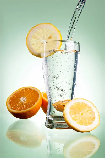 Pouring of mineral water in glass with a lemon and orange on a g — Stock Photo, Image