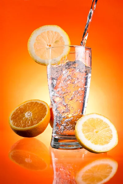 Pouring of mineral water in glass with a lemon and orange on a O — Stock Photo, Image
