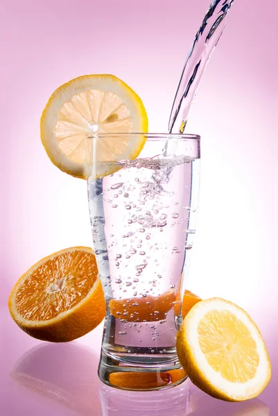Pouring of mineral water in glass with a lemon and orange on a p — Stock Photo, Image