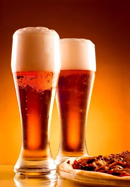 Twee glazen van bier en pizza op gele achtergrond — Stockfoto