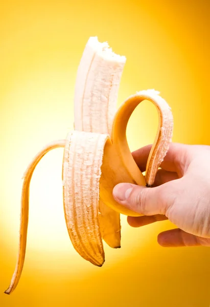 Ruka držící oloupané ukousnutý banán žluté pozadí — Stock fotografie