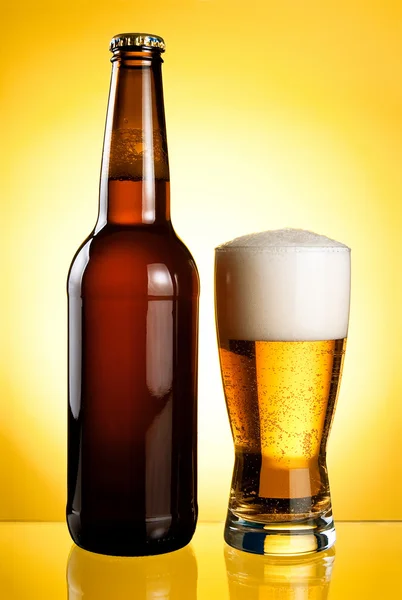 Ein Glas und eine Flasche frisches helles Bier auf gelbem Hintergrund Stockbild