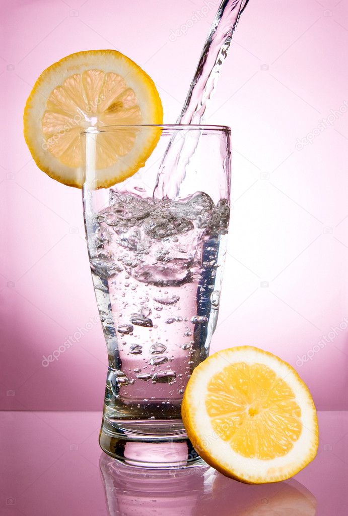 Pouring of mineral water in glass with a lemon on a pink backgro