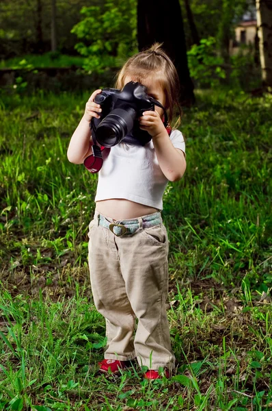 Забавная маленькая девочка фотографирует профессиональную камеру — стоковое фото