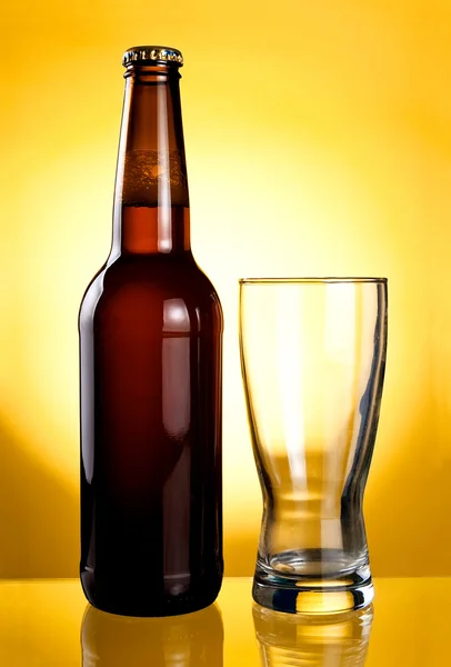 Bicchiere vuoto e bottiglia di birra marrone su uno sfondo giallo — Foto Stock