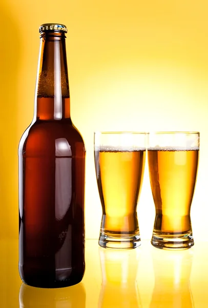 Due bicchieri e bottiglia di birra fresca leggera su sfondo giallo — Foto Stock