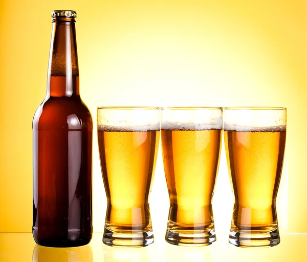 Tre bicchieri e bottiglia di birra fresca leggera su backgroun giallo — Foto Stock