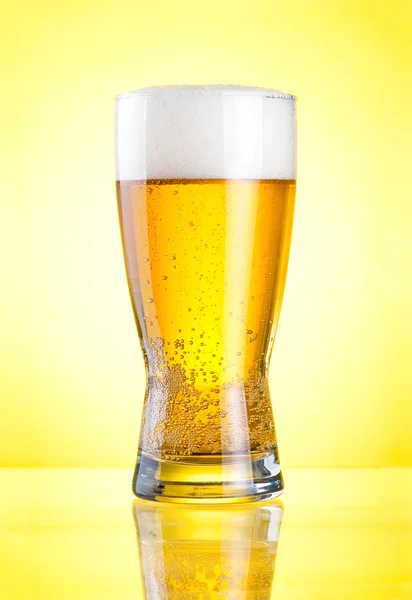 Glass of fresh lager beer close-up with froth over yellow backgr — Stock Photo, Image