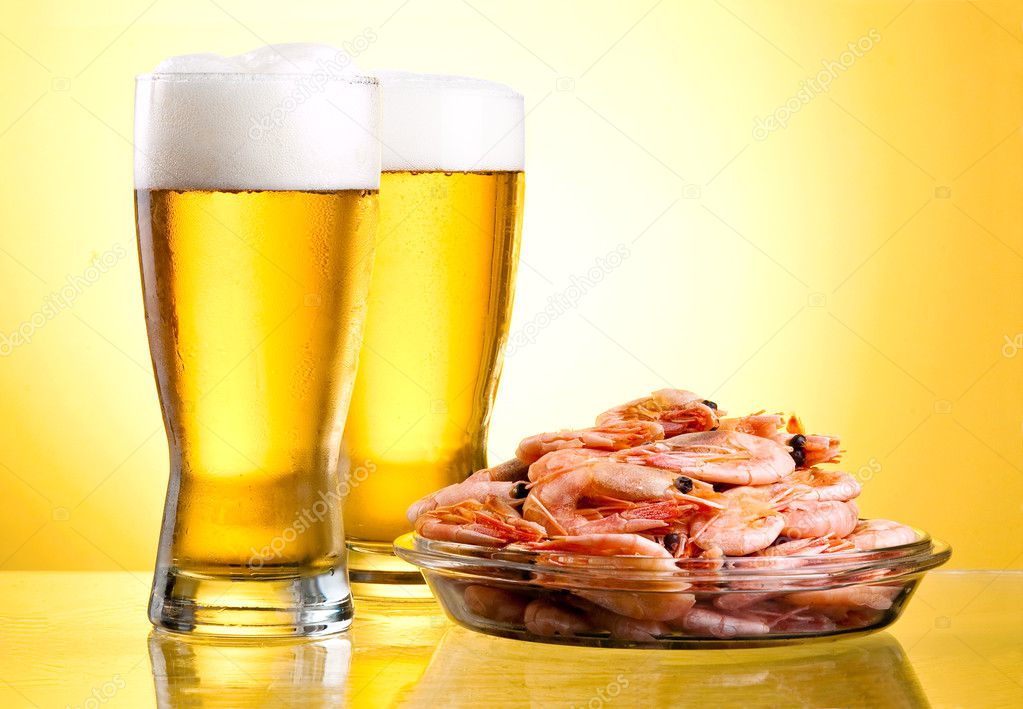 Two glass of beer and cooked shrimp on a plate on a yellow back