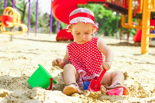 Schönes kleines Mädchen in roter Kleidung, das in einem Sandkasten spielt — Stockfoto