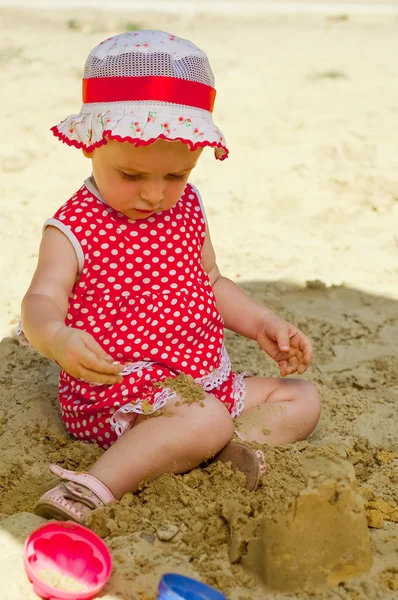 Mooi meisje in een rode kleding, spelen in een zandbak — Stockfoto