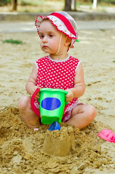 Menina bonita em roupas vermelhas, jogando em uma caixa de areia — Fotografia de Stock