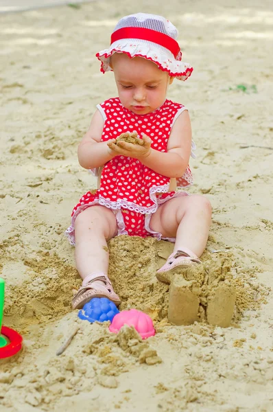 Kaunis pieni tyttö punaisissa vaatteissa, leikkii hiekkalaatikossa — kuvapankkivalokuva