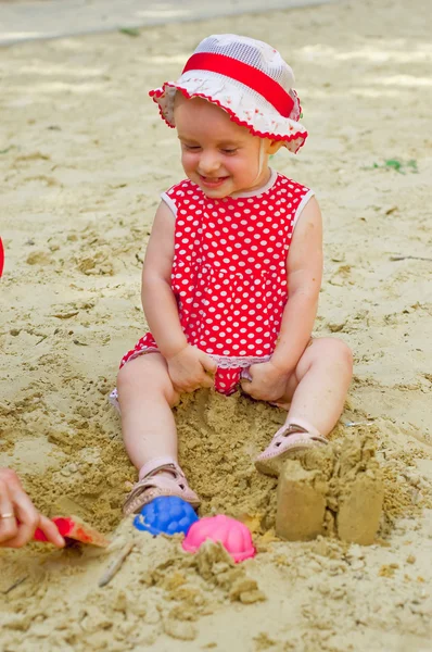 Kaunis pieni tyttö punaisissa vaatteissa, leikkii hiekkalaatikossa — kuvapankkivalokuva