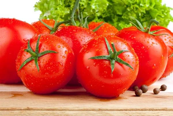 Tuoreet märät tomaatit, maustepippuri ja salaatti leikkuulaudalla — kuvapankkivalokuva