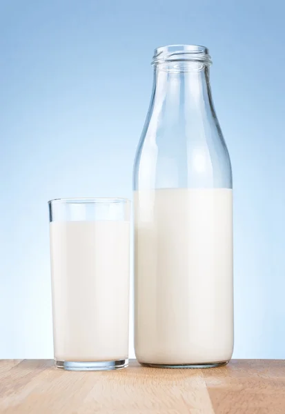 Halbe Milchflasche und Glas auf blauem Hintergrund — Stockfoto