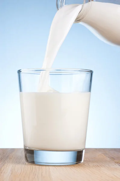 Выливание молока из бутылки в стакан на голубом фоне — стоковое фото