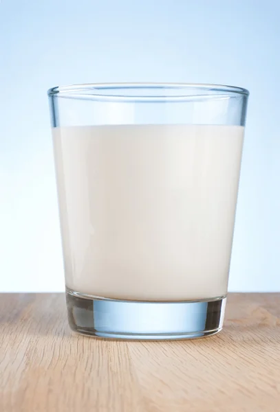 El vaso de leche fresca es una mesa de madera sobre un fondo azul — Foto de Stock