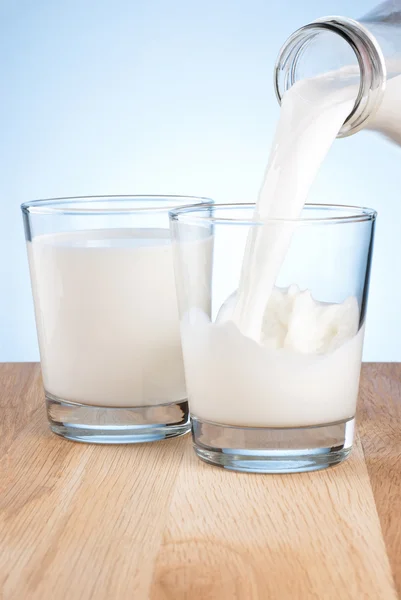 Milch aus einer Flasche in ein Zweiglas auf blauem Hintergrund gießen — Stockfoto