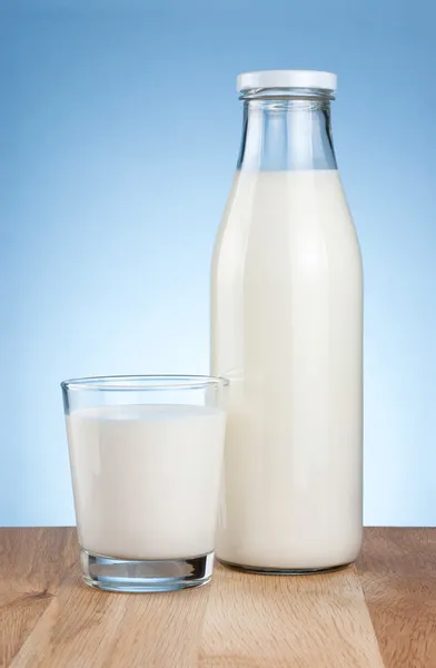 Botella de leche fresca y vidrio es una mesa de madera en un backgro azul — Foto de Stock