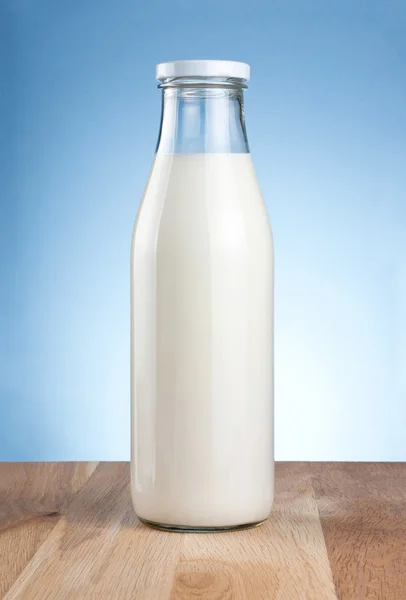 Botella de leche fresca es una mesa de madera sobre un fondo azul —  Fotos de Stock