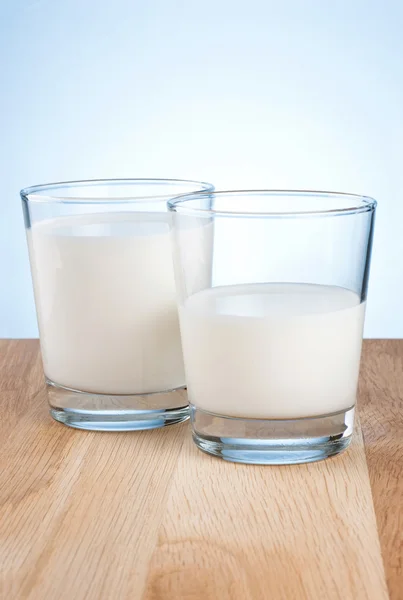 Lleno y medio vaso de leche fresca está en la mesa de madera un fondo azul — Foto de Stock
