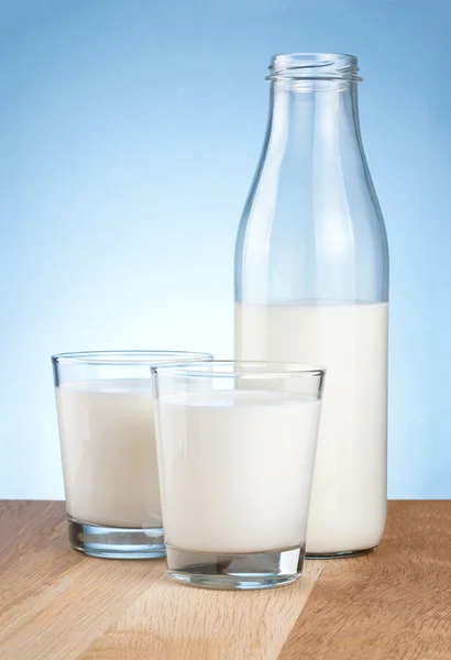 Láhev půl mléka a dvě skla je dřevěný stůl na modré backgro — Stock fotografie