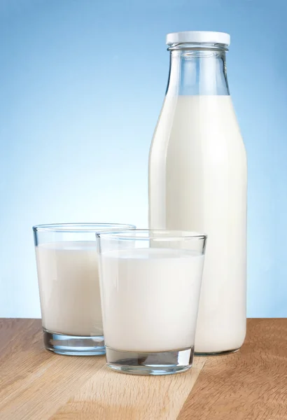 Garrafa cheia de leite fresco e dois copos é mesa de madeira em um blu — Fotografia de Stock