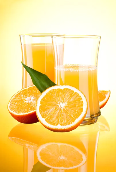 Two Glasses of Fresh Orange juice, half oranges and the leaves o — Stock Photo, Image