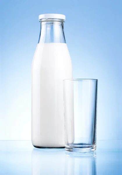 Бутылка свежего молока и чистый стакан на синем фоне — стоковое фото