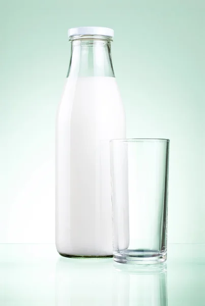 Flasche frische Milch und leeres Glas auf grünem Hintergrund — Stockfoto