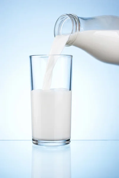 Despejar leite de uma garrafa em um copo em um fundo azul — Fotografia de Stock