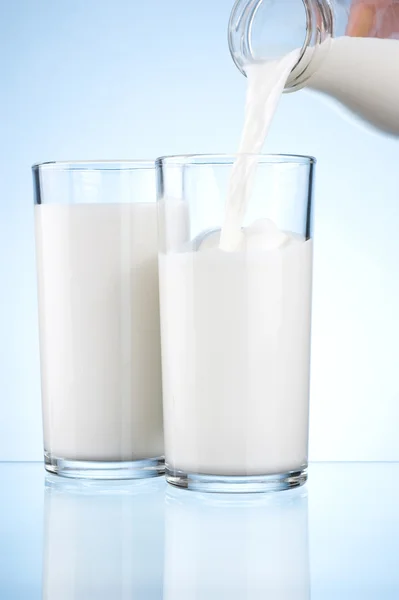 Versare il latte da una bottiglia nei due bicchieri su uno schienale blu — Foto Stock