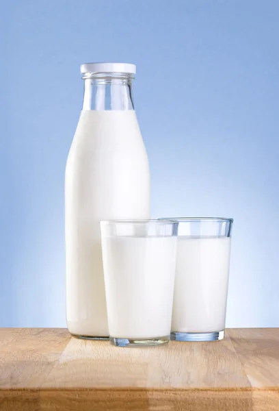 Full flaska av färsk mjölk och två glas är träbord på en blu — Stockfoto