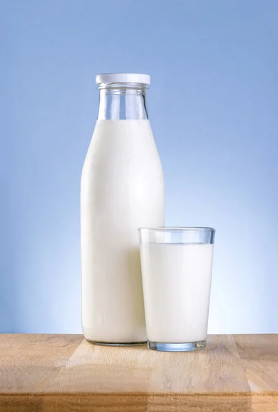 Bottle of fresh milk and glass is wooden table on a blue backgro — Stock Photo, Image