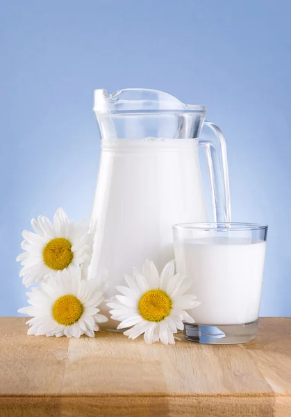 Karaf verse melk, glas en drie kamille bloemen is houten tabl — Stockfoto