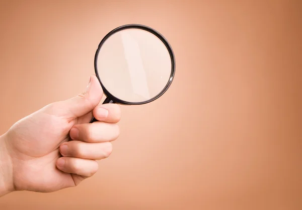 Hand holding magnifying glass on the beige background — Stock Photo, Image